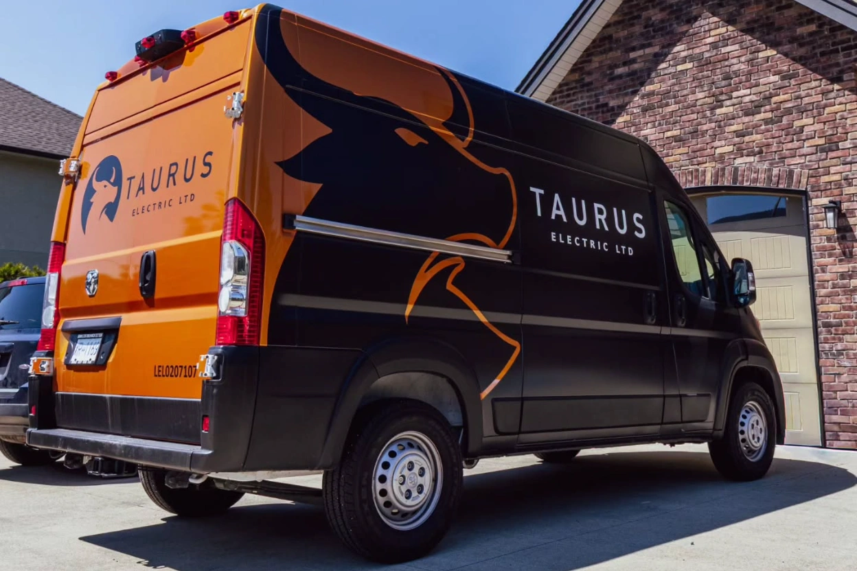 A Taurus Electric van, wrapped in orange and black with the bull logo, parked in an Abbotsford driveway.