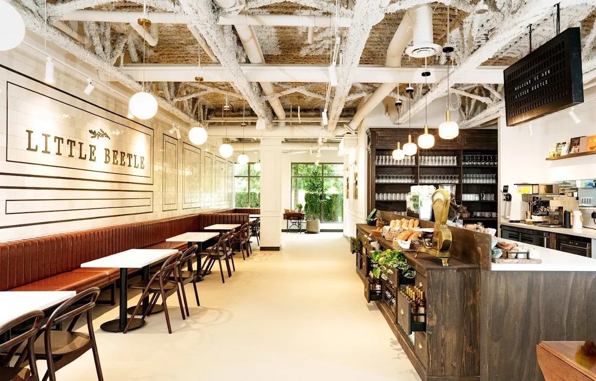 Modern café interior with white walls, exposed ceiling, pendant lights, brown seating and wooden tables — an example of Taurus Electric's work.