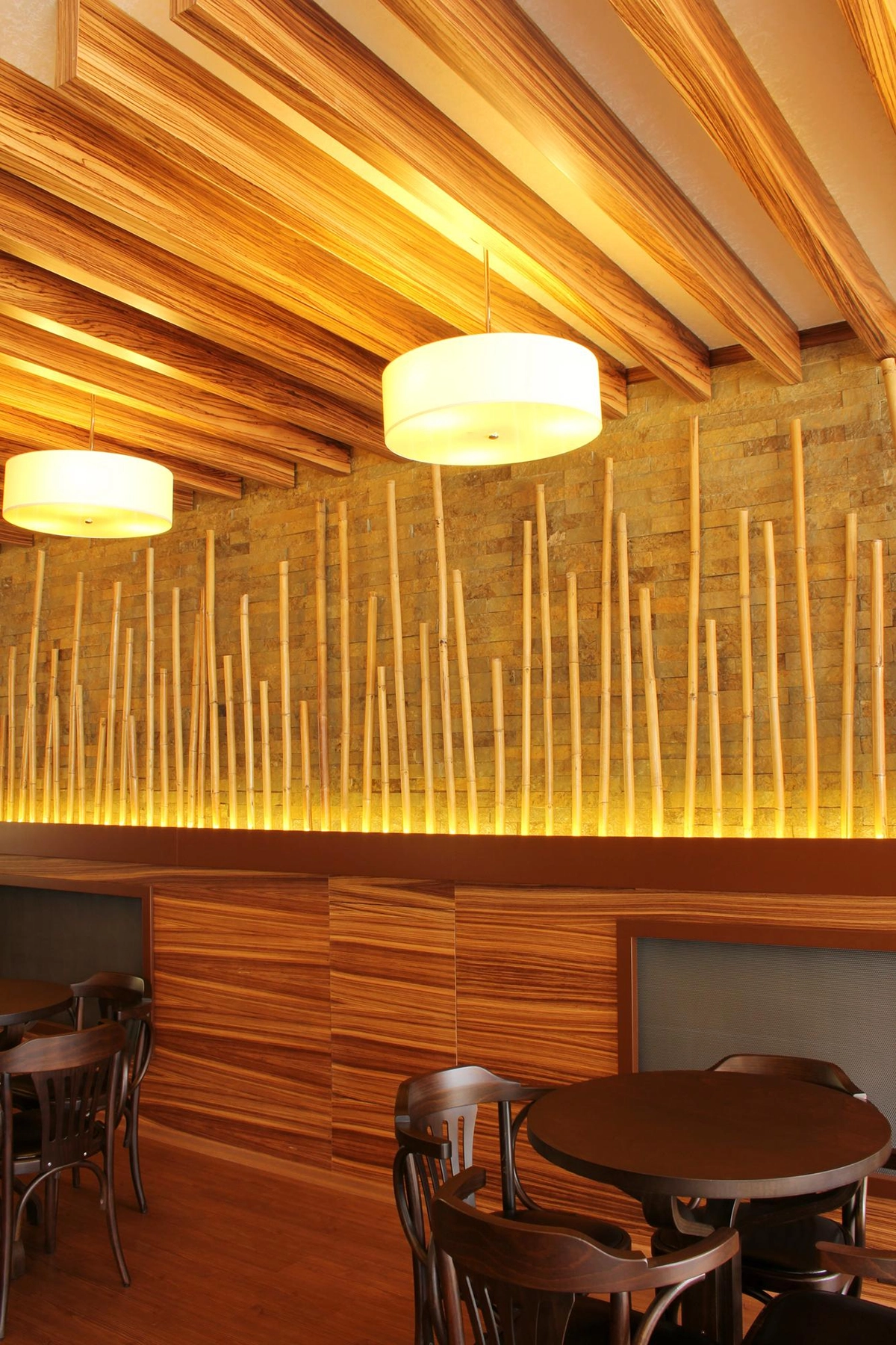 A restaurant interior with wooden decor, round dark tables and chairs, and a wood-panelled wall.