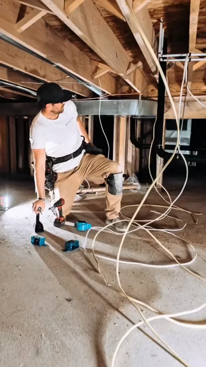 A Taurus Electric electrician running wire through a crawlspace under floor joists during a Langley build.