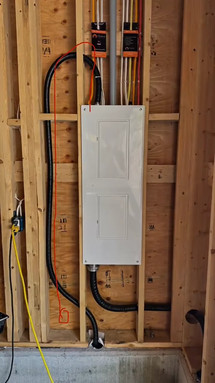 A new electrical panel mounted on open stud framing during a Mission build, with conduit and branch circuits run in to it.