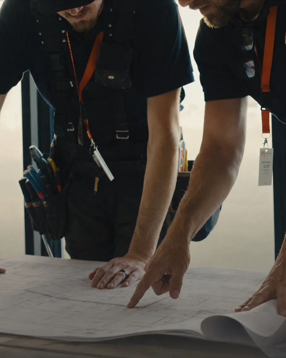 Two Taurus Electric electricians in branded polos leaning over a set of drawings together on site.